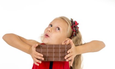 little beautiful female child in red dress holding happy delicious chocolate bar in her hands eating delighted
