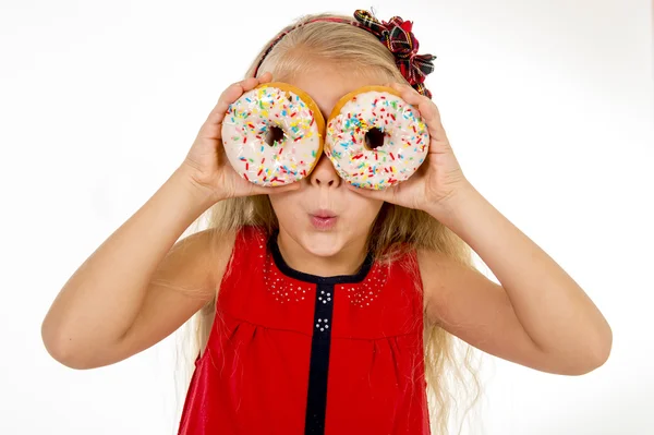 Enfant femelle avec de longs cheveux blonds et robe rouge jouant avec deux beignet de sucre avec garnitures les mettant comme des yeux — Photo