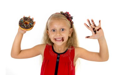 beautiful female child with blue eyes in cute red dress eating chocolate donut with syrup stains