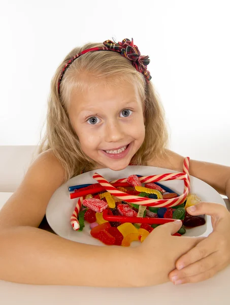 Bastante pequeño niño femenino comer plato lleno de caramelo caramelo y alimentos dulces en el abuso de azúcar y dieta poco saludable — Foto de Stock