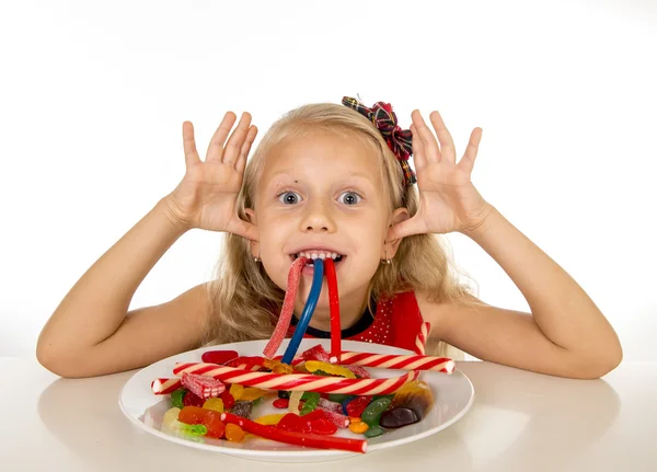 Pretty little female child eating dish full of candy caramel and sweet food in sugar abuse and unhealthy diet — Stockfoto