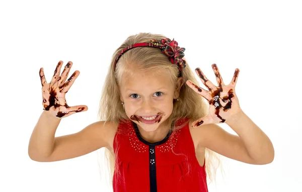 Pretty little female child with long blond hair and blue eyes wearing red dress showing dirty hands with stains of chocolate syrup — Stock Photo, Image