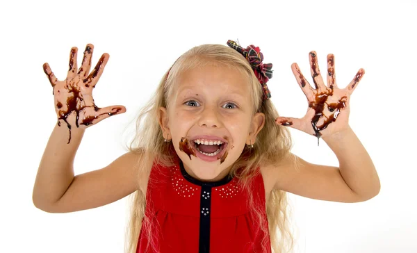 Pretty little female child with long blond hair and blue eyes wearing red dress showing dirty hands with stains of chocolate syrup — Zdjęcie stockowe