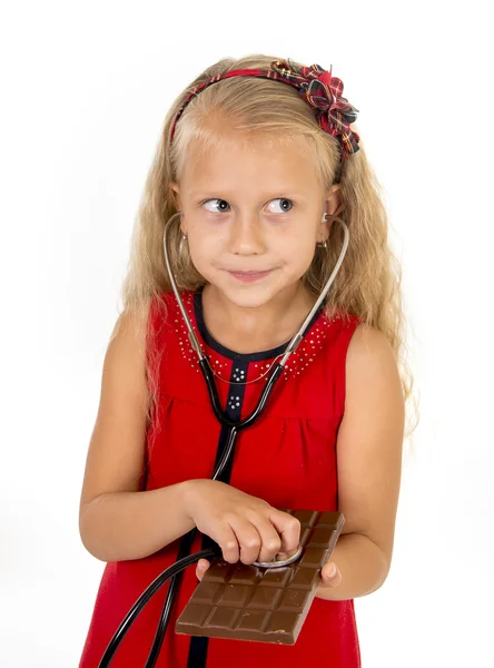 Pretty little female child with stethoscope on chocolate bar looking worried in unhealthy nutrition habit — Stock Photo, Image