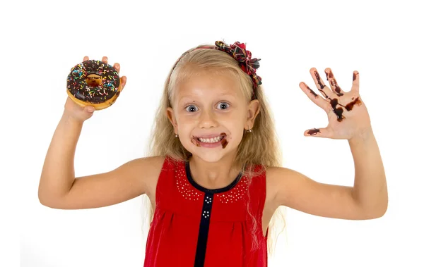 Beautiful female child with blue eyes in cute red dress eating chocolate donut with syrup stains — Zdjęcie stockowe