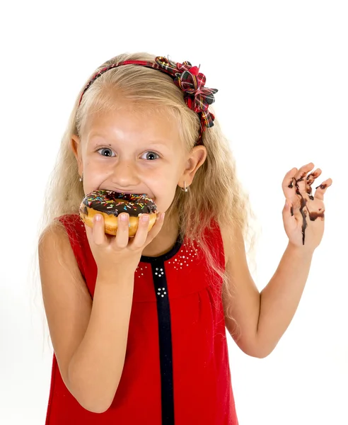 Beautiful female child with blue eyes in cute red dress eating chocolate donut with syrup stains — Zdjęcie stockowe