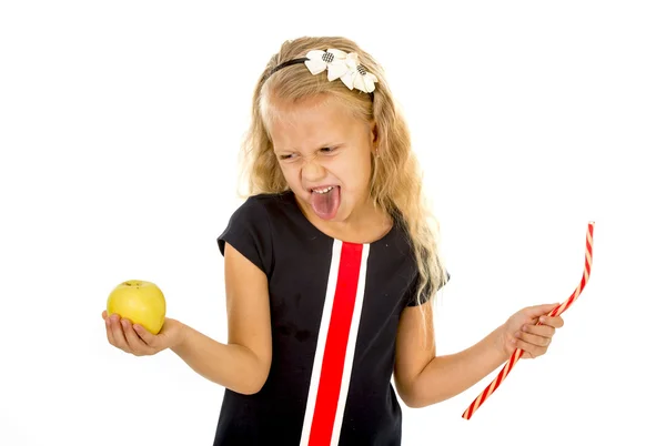Маленька красива дівчинка, яка вибирає десерт, тримає нездорову, але смачну червону цукерку солодощі та яблучні фрукти — стокове фото