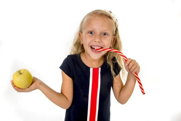 Little pretty female child choosing dessert holding unhealthy but tasty red candy licorice and apple fruit — Stock Photo, Image