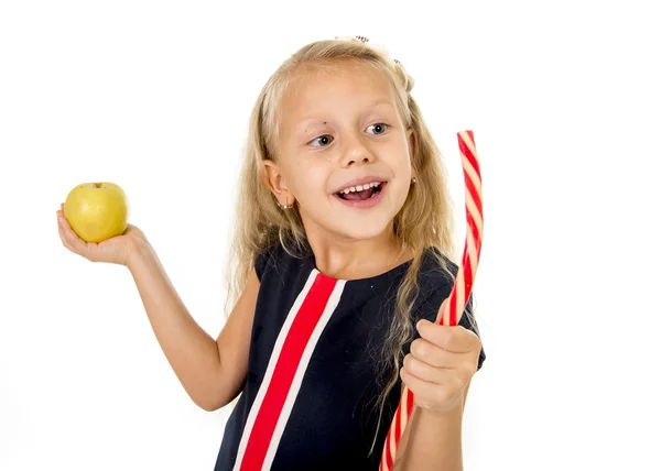 Little pretty female child choosing dessert holding unhealthy but tasty red candy licorice and apple fruit — 스톡 사진