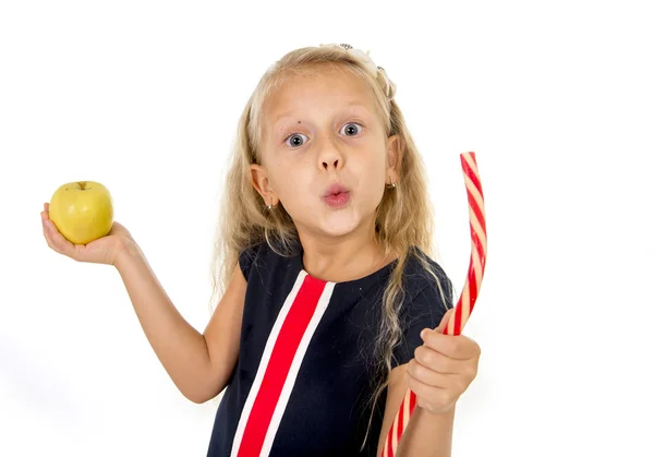Little pretty female child choosing dessert holding unhealthy but tasty red candy licorice and apple fruit — ストック写真
