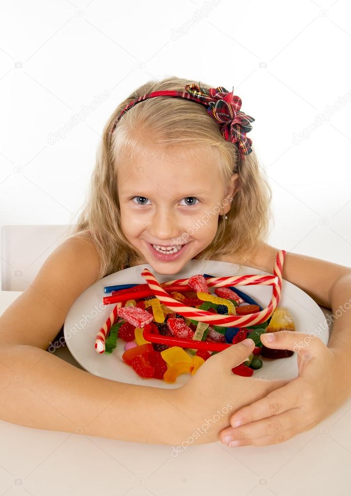 pretty little female child eating dish full of candy caramel and sweet food in sugar abuse and unhealthy diet