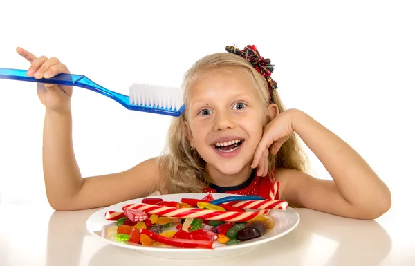Anak perempuan lucu makan hidangan penuh permen dan memegang sikat gigi besar dalam perawatan gigi dan konsep kesehatan — Stok Foto