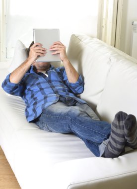 young attractive 30s man using digital tablet pad lying on couch at home networking looking relaxed