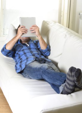 young attractive 30s man using digital tablet pad lying on couch at home networking looking relaxed clipart