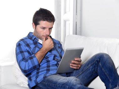 young attractive 30s man using digital tablet pad lying on couch at home networking looking relaxed