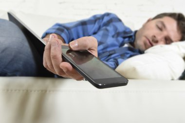 young attractive tired and overworked falling asleep at home couch with mobile phone and digital tablet pad
