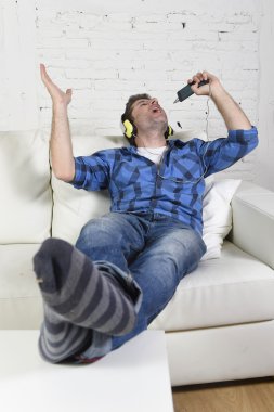 happy crazy man on couch listening to music holding mobile phone as microphone