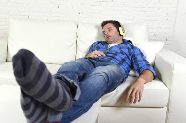 man falling asleep on home couch while listening to music with mobile phone and headphones