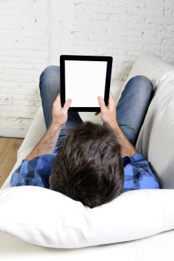 man lying on home couch using digital tablet pad in portable internet technology