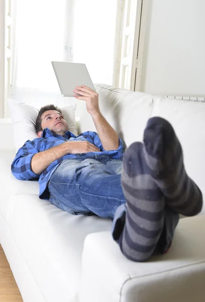 Young attractive 30s man using digital tablet pad lying on couch at home networking looking relaxed — Stockfoto