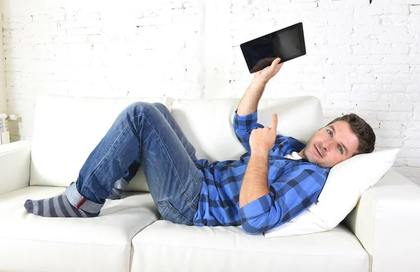 Young attractive 30s man using digital tablet pad lying on couch at home networking looking relaxed — Stockfoto