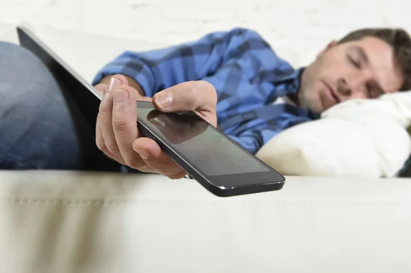 Joven atractivo cansado y sobrecargado de trabajo quedarse dormido en el sofá de casa con teléfono móvil y tableta digital —  Fotos de Stock