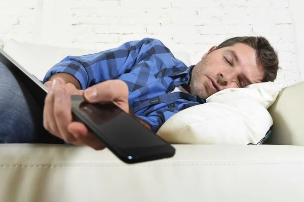 Joven atractivo cansado y sobrecargado de trabajo quedarse dormido en el sofá de casa con teléfono móvil y tableta digital —  Fotos de Stock