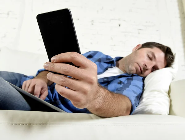 Young attractive tired and overworked falling asleep at home couch with mobile phone and digital tablet pad — Stock fotografie