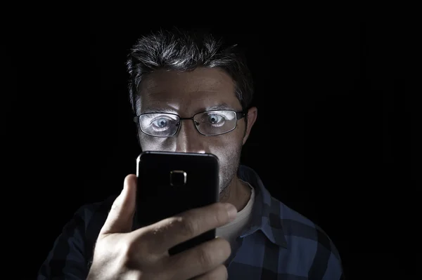 Close up portrait of young man looking intensively to mobile phone screen with blue eyes wide open isolated on black background — Stock fotografie