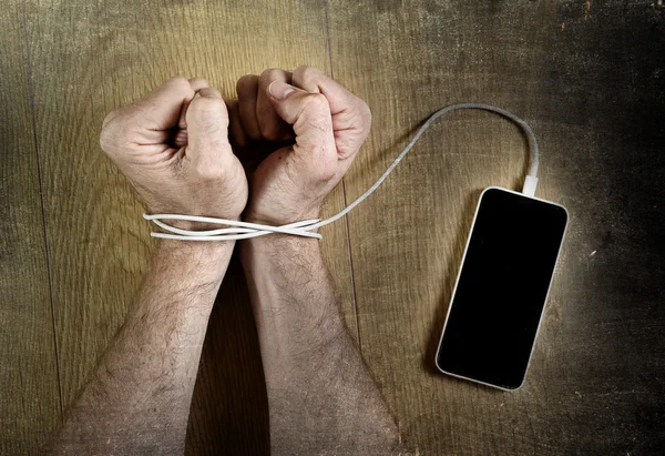 Man hands wrapped on wrists with mobile phone cable handcuffed in smart phone networking addiction concept — Stock Photo, Image