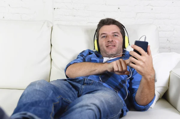 Man having fun alone lying on home couch listening to music with mobile phone and headphones — Stok fotoğraf