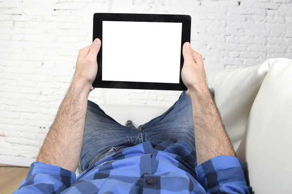 Man lying on home couch using digital tablet pad in portable internet technology — Stockfoto