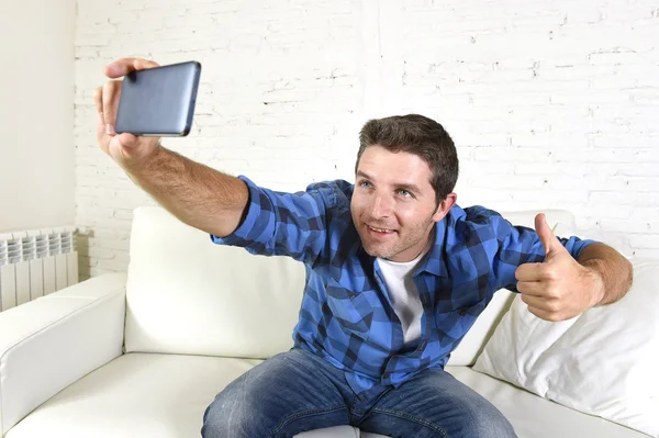 Молодой привлекательный 30-х мужчина делает селфи фото или видео с мобильного телефона дома, сидя на диване улыбаясь счастливой — стоковое фото
