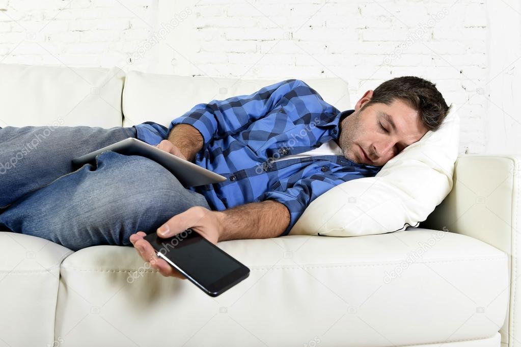 attractive man sleeping at home couch with mobile phone and digital tablet pad in his hands