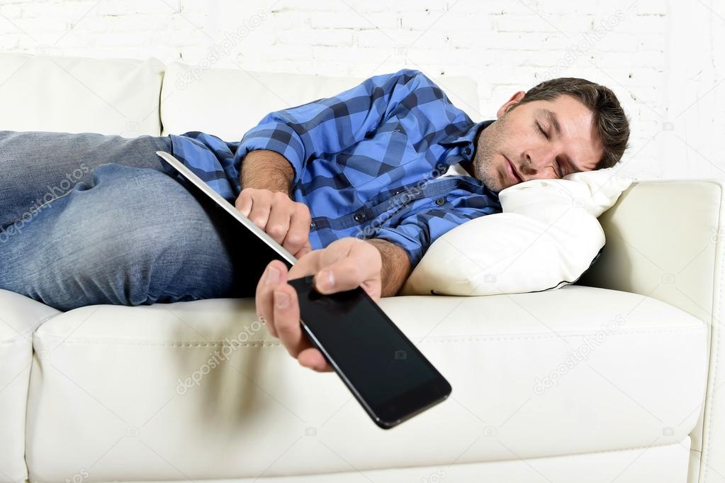 attractive man sleeping at home couch with mobile phone and digital tablet pad in his hands