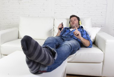 young attractive man having fun alone lying on couch listening to music with mobile phone and headphones