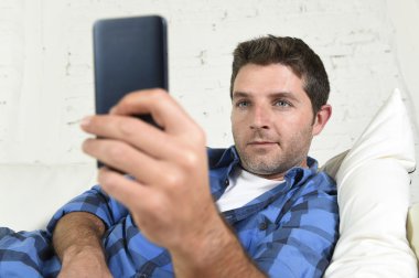 young attractive man lying relaxed at home couch texting and surfing on internet in his mobile phone