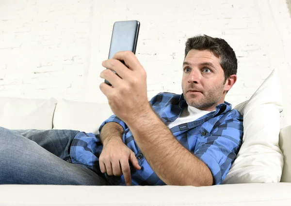 Jeune homme attrayant couché détendu à la maison canapé textos et surf sur Internet dans son téléphone mobile — Photo