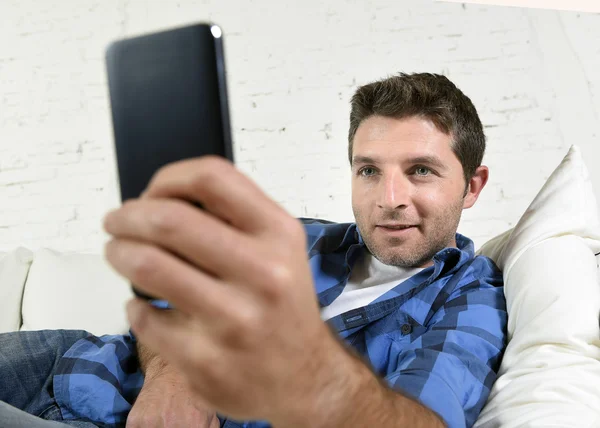 Young attractive man lying relaxed at home couch texting and surfing on internet in his mobile phone — Stock Fotó