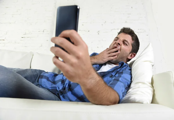 Joven atractivo cansado y sobrecargado de trabajo quedarse dormido bostezando en el sofá de casa con teléfono móvil y tableta digital — Foto de Stock