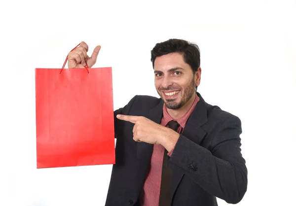 Joven atractivo hombre de negocios sosteniendo y señalando bolsa de compras roja en concepto de venta que actúa como vendedor — Foto de Stock