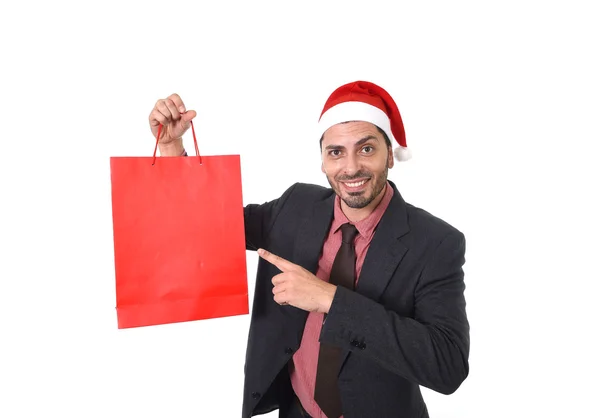 Young attractive businessman in Christmas Santa hat holding and pointing red shopping bag in December and New year sale — 图库照片