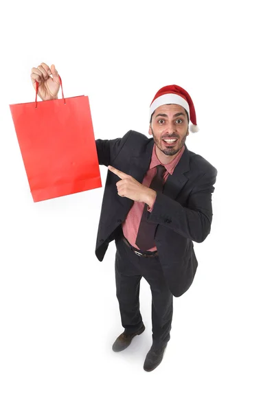 Young attractive businessman in Christmas Santa hat holding and pointing red shopping bag in December and New year sale — Stock Photo, Image