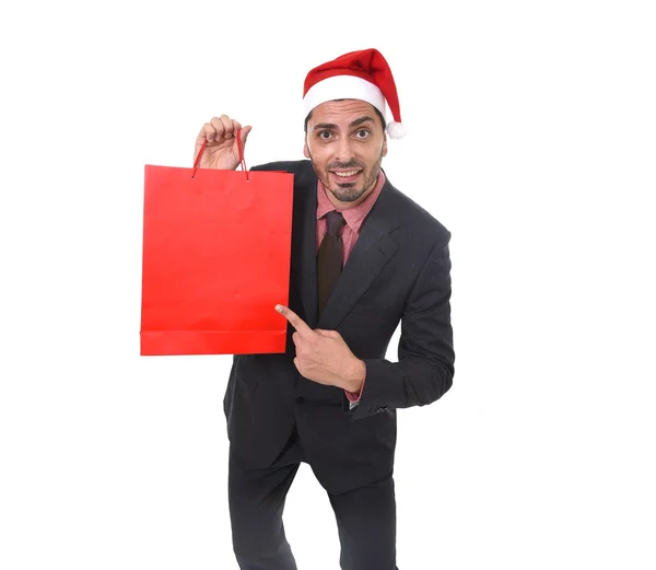 Young attractive businessman in Christmas Santa hat holding and pointing red shopping bag in December and New year sale — Stockfoto