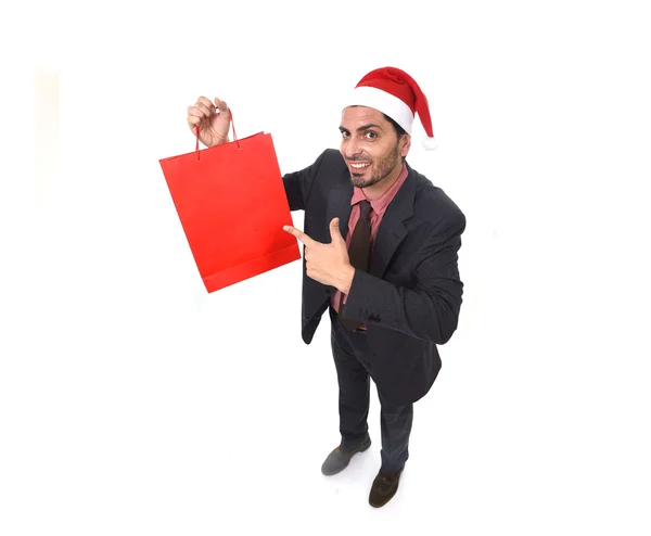 Jovem atraente empresário no Natal Santa chapéu segurando e apontando saco de compras vermelho em dezembro e venda de ano novo — Fotografia de Stock