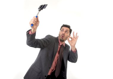 young attractive businessman in suit and tie taking selfie photo with mobile phone camera and stick posing happy