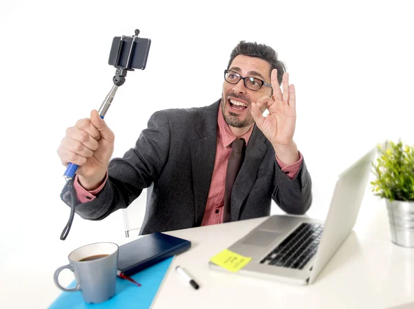 Funny nerd businessman at office desk taking selfie photo with mobile phone camera and stick — Zdjęcie stockowe