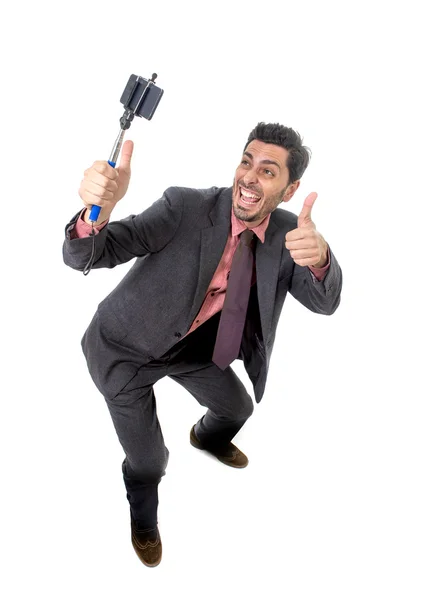 Joven atractivo hombre de negocios en traje y corbata tomando foto selfie con la cámara del teléfono móvil y palo posando feliz —  Fotos de Stock