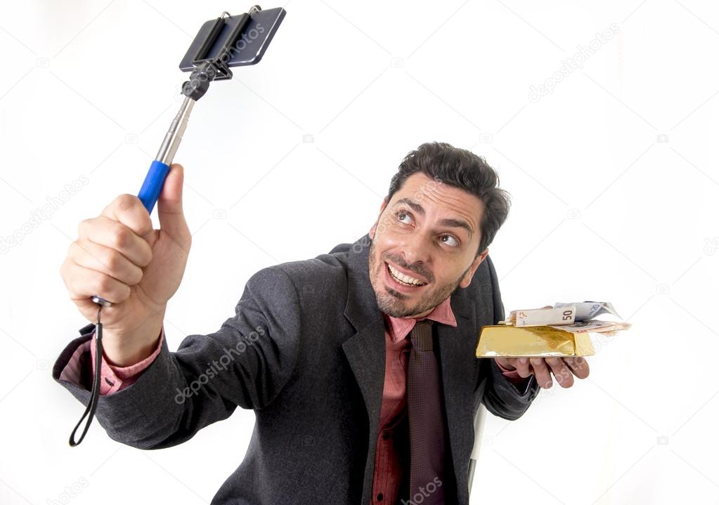 businessman taking selfie photo with mobile phone camera and stick posing happy and successful with gold bar and money