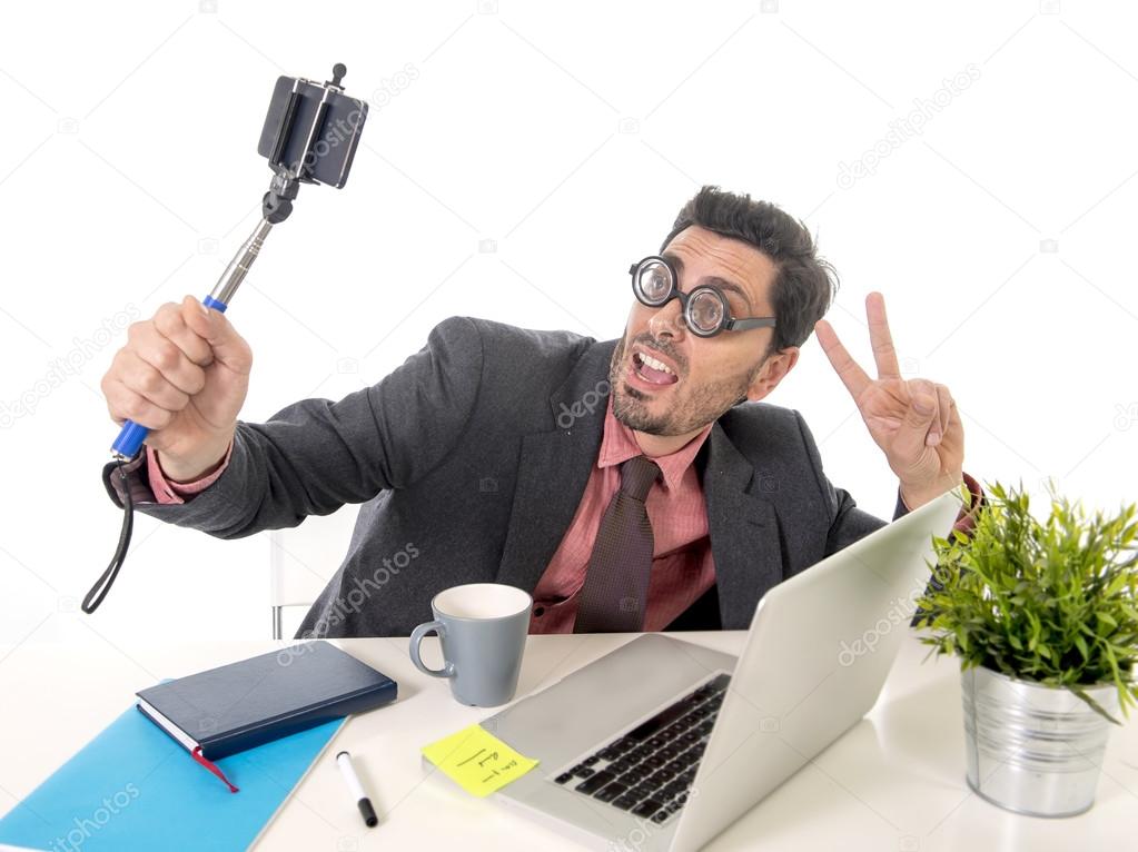 funny nerd businessman at office desk taking selfie photo with mobile phone camera and stick